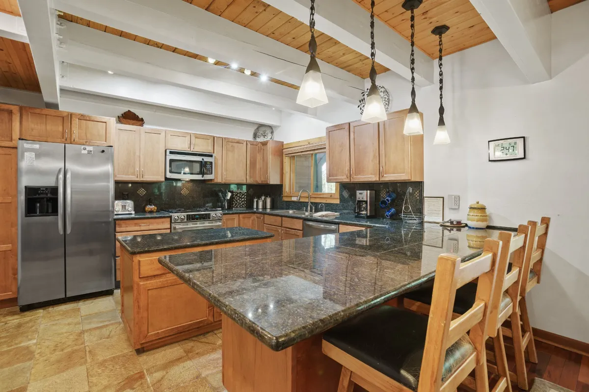 A modern kitchen with a prominent granite countertop, wooden cabinetry, and a central island, illuminated by recessed lighting. The layout is ideal for cooking, entertaining, and gathering as a group.