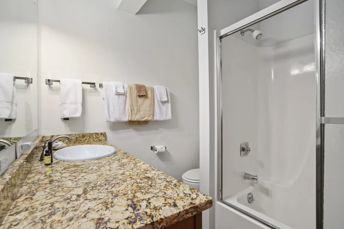 A spa-inspired bathroom featuring a granite countertop, large mirror, modern shower area, and plush towels. The clean lines and muted tones evoke a sense of calm and relaxation.