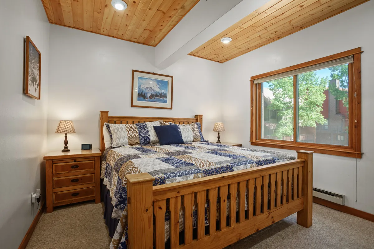 A warmly lit bedroom with a comfortable bed, nightstand, window, and inviting artwork. The room's soft colors and subtle decor cultivate a restful and inviting environment.
