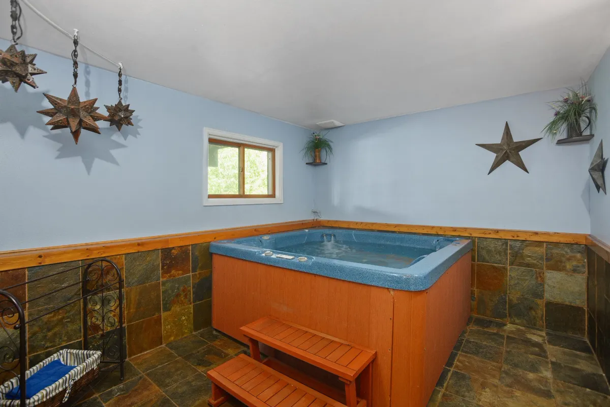 This image features a tranquil interior hot tub area with wooden steps leading into the water, slate flooring, and subtle wall decor. The ambiance suggests a relaxing, spa-like retreat perfect for unwinding and socializing after a day outdoors.