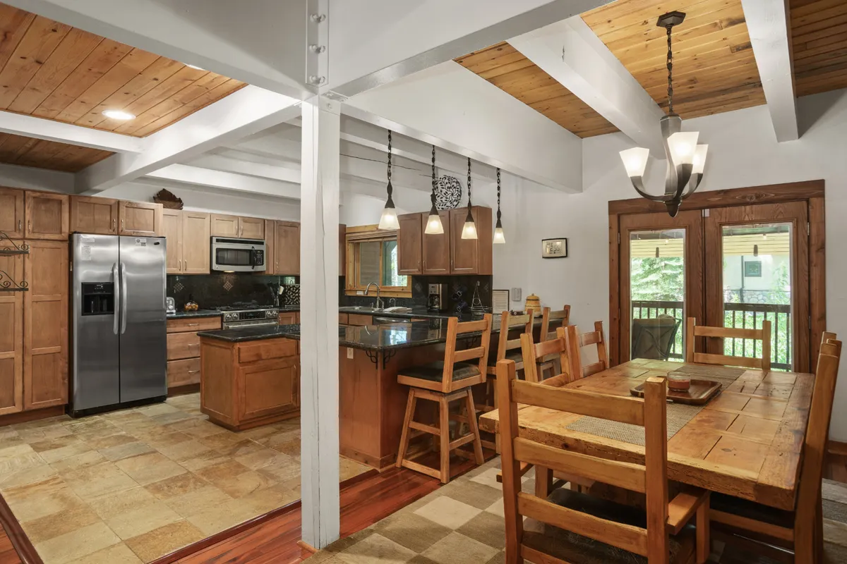 A cohesive view of the kitchen and dining area, featuring a spacious kitchen island, a large dining table set for a group, elegant hanging light fixtures, and warm wooden cabinetry. The open plan allows for easy movement and conversation between spaces, embodying the section’s focus on connection and shared experiences.