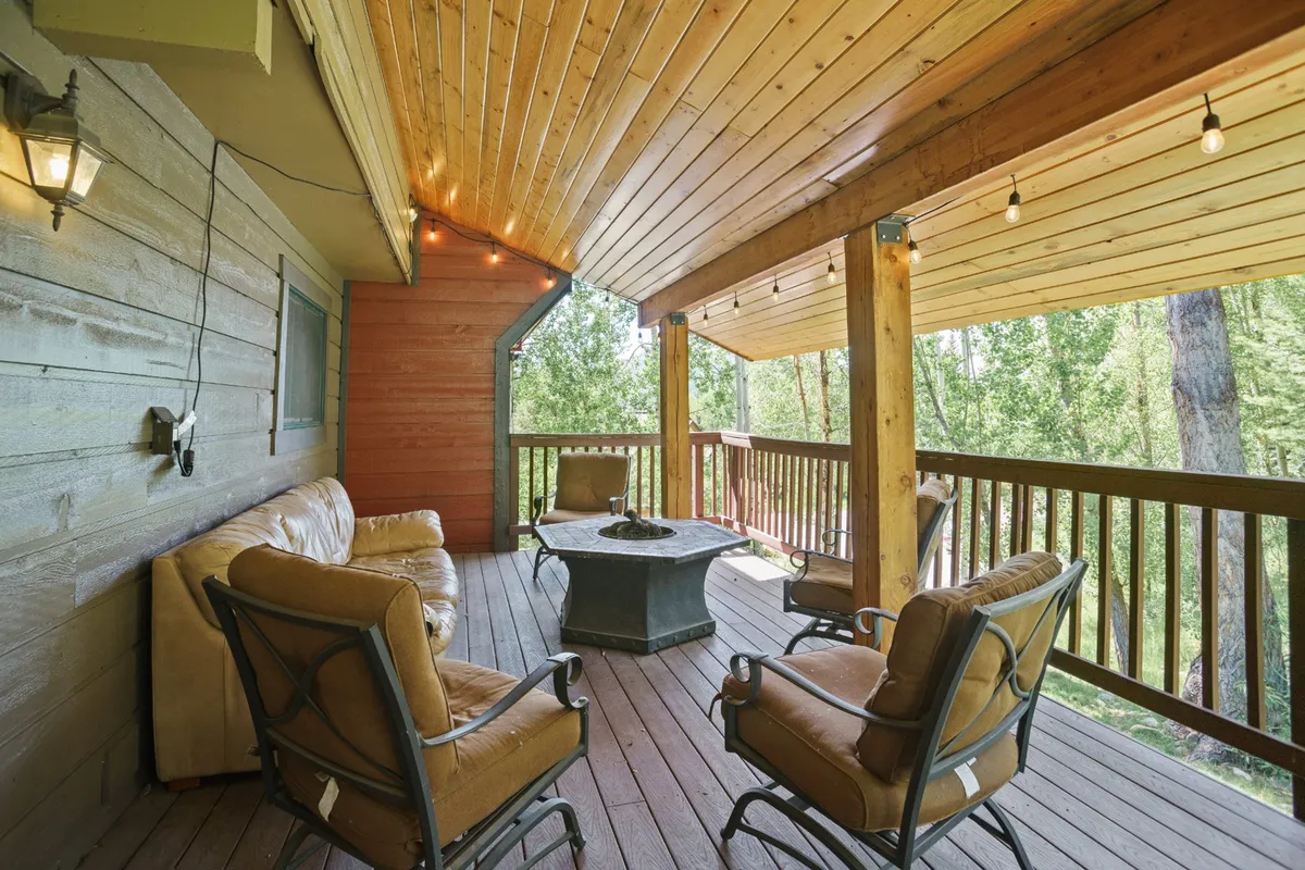 An inviting outdoor lounge with a fire pit and comfortable seating beneath a wooden ceiling, surrounded by mature trees. The scene highlights a magical winter evening ambiance, perfect for unwinding after a day on the mountain.