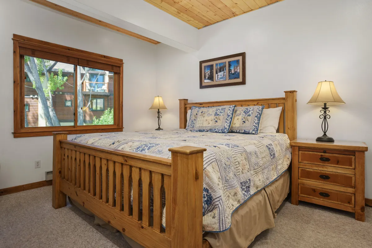 A bright, inviting bedroom with a comfortable bed positioned near a large window, flanked by lamps and accented with framed pictures. The window allows natural light to fill the room, reinforcing themes of relaxation and a welcoming atmosphere suitable for long-term guests.