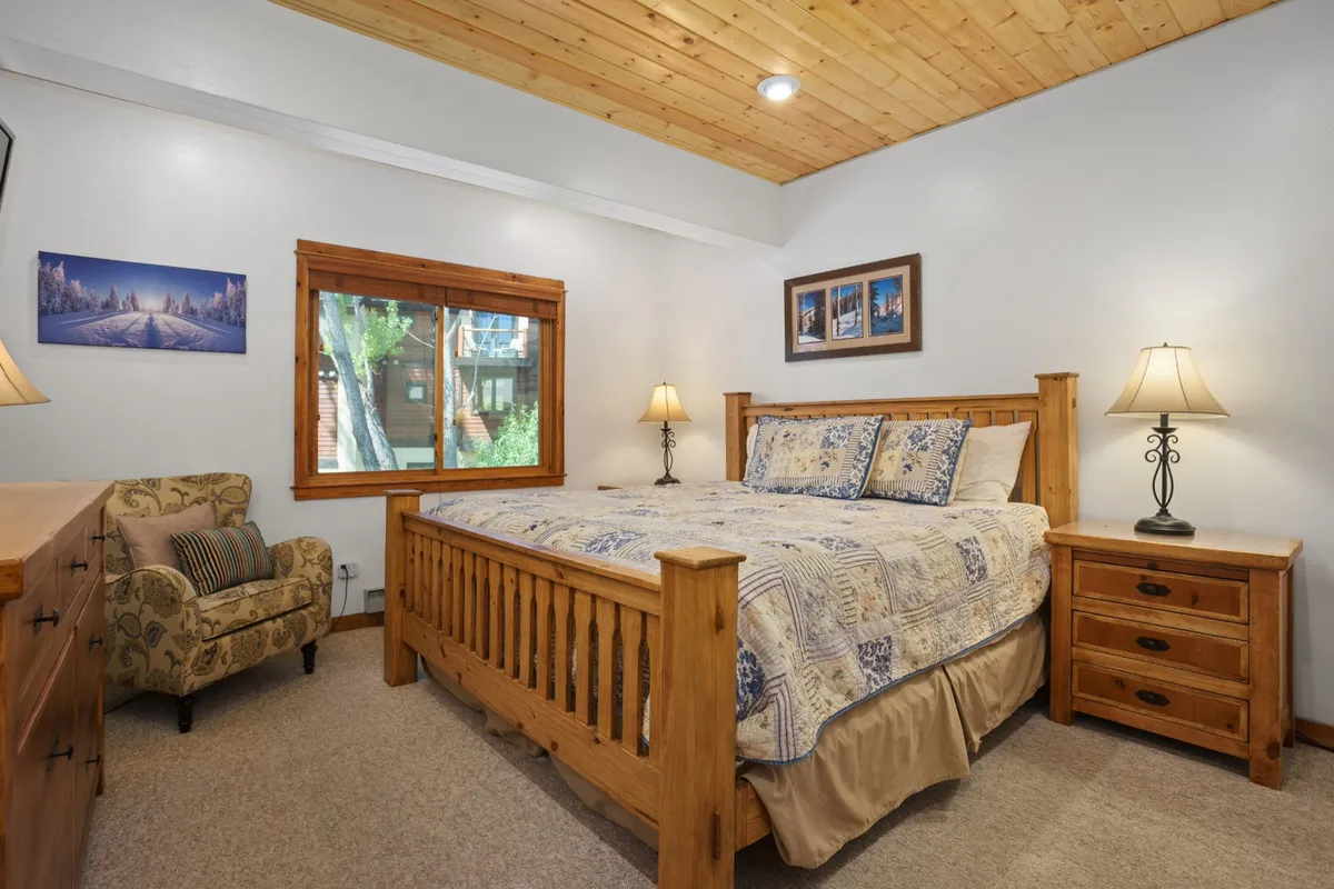 A serene bedroom featuring a cozy bed positioned next to a large window that lets in ample natural light. An armchair by the window and a nightstand with a lamp create a comfortable reading nook, while the tasteful decor contributes to a peaceful atmosphere.