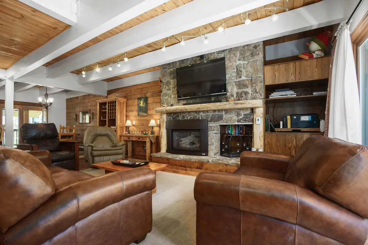 A warm and inviting living room anchored by a stone fireplace, flanked by comfortable leather sofas and wooden shelving. The TV above the fireplace invites movie nights, while the space is perfect for relaxing after outdoor adventures.