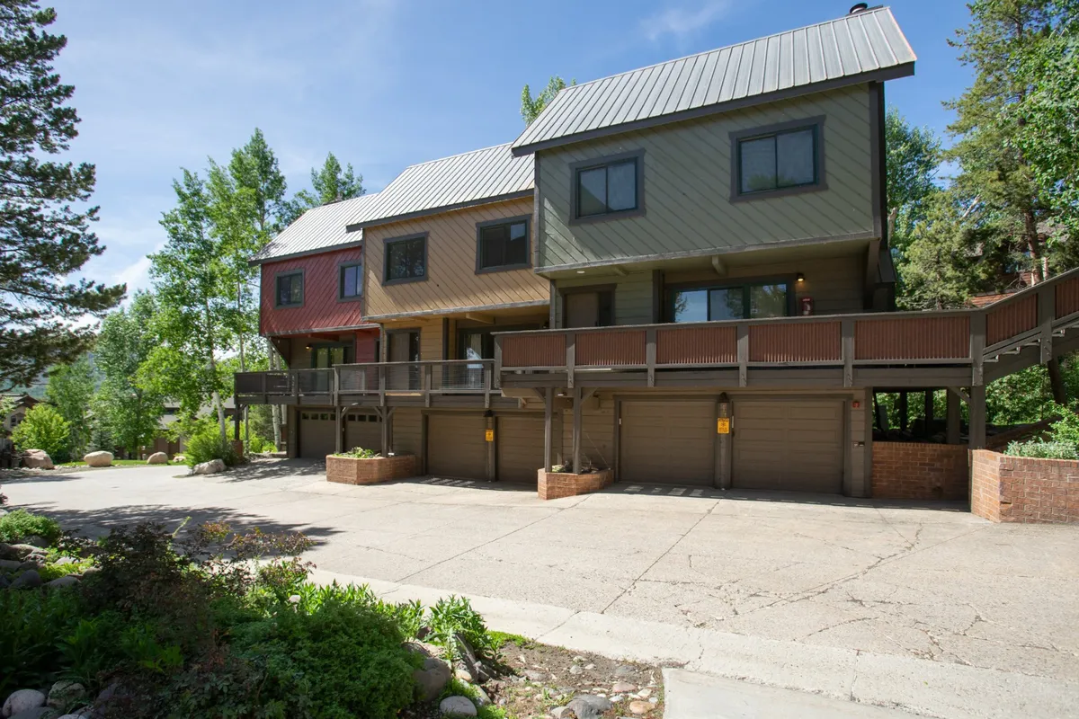 This exterior image features three distinct houses with wooden decks, set among mature green trees. The decks provide opportunities for outdoor gatherings, family barbecues, and enjoying the surrounding nature, with proximity to hiking trails and scenic views.