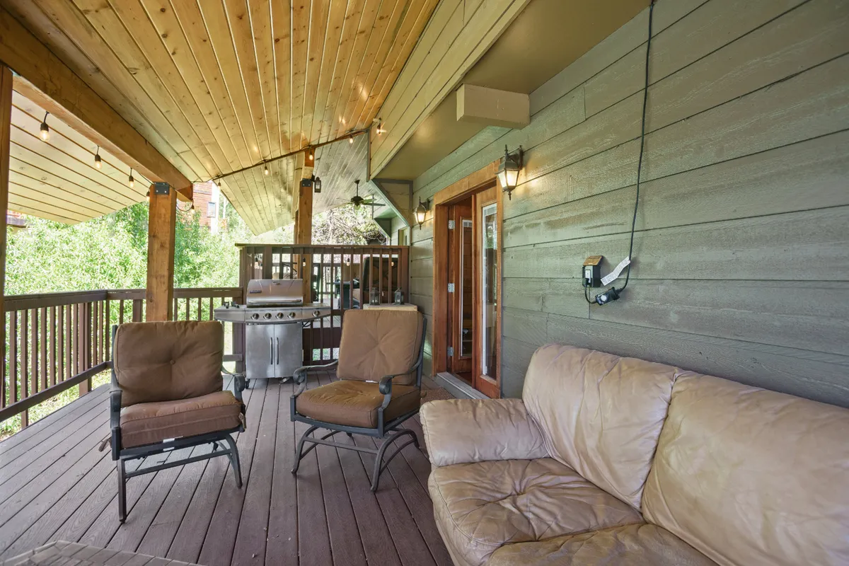 A covered deck area with comfortable outdoor seating, a barbecue grill, and a wooden railing, suggesting a relaxed space for dining or sipping morning coffee while enjoying the natural surroundings.