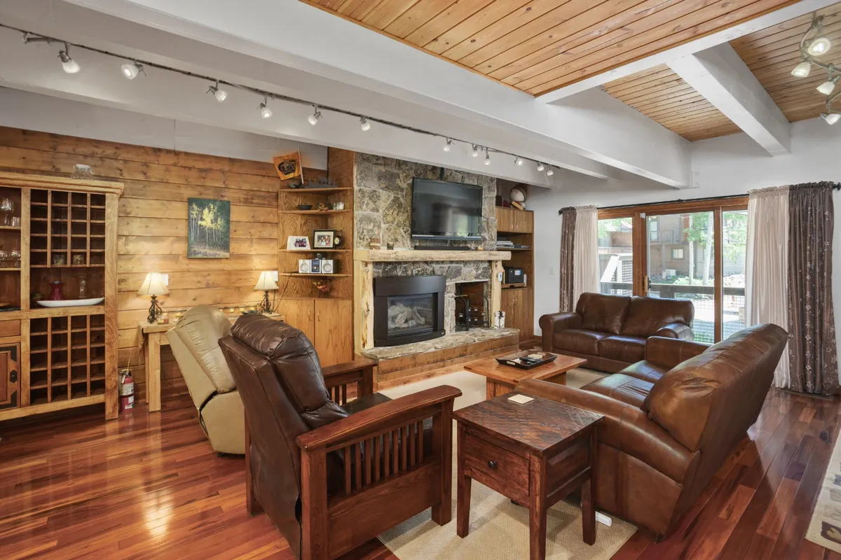 The image showcases a spacious, inviting living area anchored by a grand stone fireplace, surrounded by plush, comfortable seating and built-in wooden shelves. Natural light streams in through large windows, creating a warm, welcoming setting perfect for relaxation and togetherness.